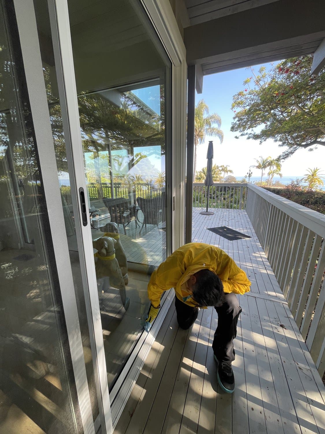 Squeegee Crew technician cleaning a sliding glass door on an ocean-view deck in the 805
