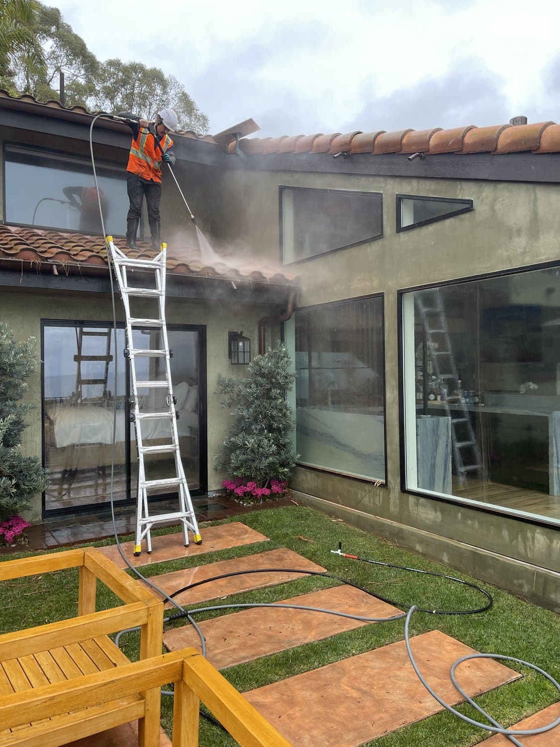 Squeegee Crew technician pressure washing a tile roof from a ladder in the 805